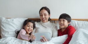 침대에서 아이와 함께 태블릿으로 동화를 읽는 따뜻한 분위기의 부모와 아이